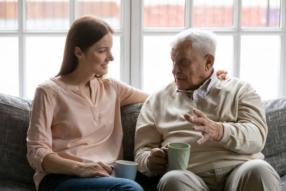 Adult daughter talking with aging dad on couch